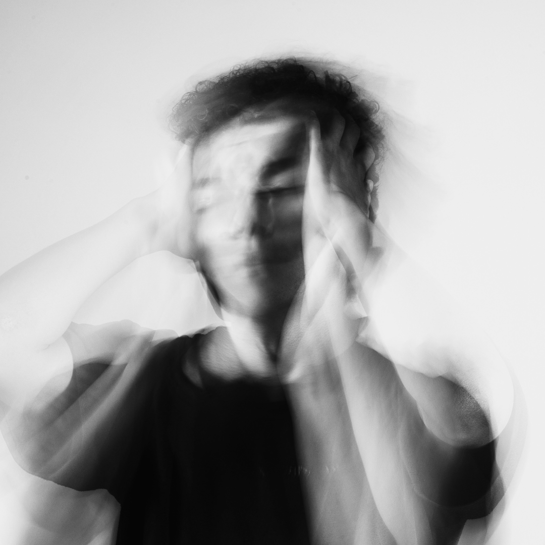 Schwarz-weiß Bild eines Mannes, dessen Gesicht verschwommen dargestellt ist, während er sich die Hände an den Kopf hält – symbolisiert Stress und Leistungsdruck.
